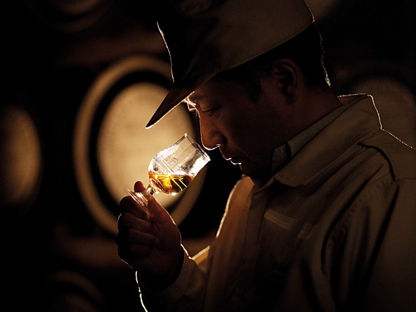 Man smelling a small glass of amber coloured alcohol